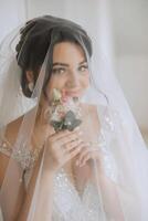 moda foto di un' bellissimo sposa con buio capelli nel un elegante nozze vestito e sbalorditivo trucco nel il camera su il mattina di il nozze. il sposa è preparazione per il nozze