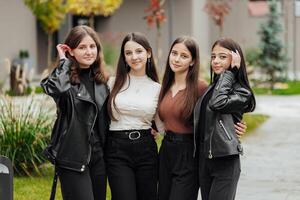 gruppo di sorridente e contento adolescenziale amici indossare casuale Abiti la spesa tempo insieme, in posa e parlando con ogni altro vicino Università edificio su autunno giorno. foto