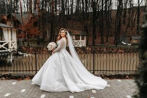 bellissimo sposa con un' nozze mazzo di fiori, attraente donna nel un' nozze vestito con un' lungo velo. contento sposa donna. sposa con nozze trucco e pettinatura. inverno nozze foto