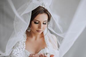 moda foto di un' bellissimo sposa con buio capelli nel un elegante nozze vestito e sbalorditivo trucco nel il camera su il mattina di il nozze. il sposa è preparazione per il nozze