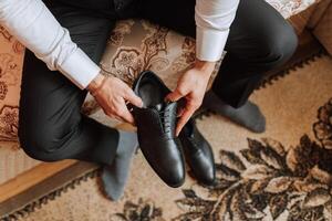 un elegante uomo indossa nero pelle formale scarpe. legatura scarpe. attività commerciale uomo legatura lacci delle scarpe su il pavimento. su vicino il sposo è preparazione per il nozze. foto