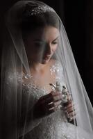 moda foto di un' bellissimo sposa con buio capelli nel un elegante nozze vestito e sbalorditivo trucco nel il camera su il mattina di il nozze. il sposa è preparazione per il nozze