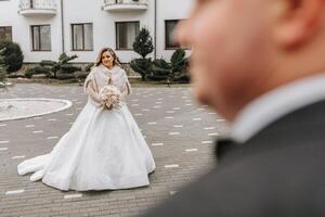 il sposa e sposo siamo a piedi vicino il Hotel e in posa, contento e godendo il giorno, Tenere mani. un' lungo treno su il vestire. inverno nozze foto