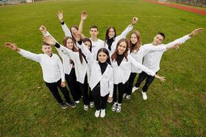 un' gruppo di molti contento adolescenti vestito nel il stesso attrezzatura avendo divertimento e in posa nel un' stadio vicino un' Università. concetto di amicizia, momenti di felicità. scuola amicizia foto