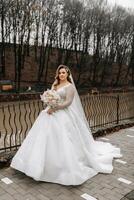 bellissimo sposa con un' nozze mazzo di fiori, attraente donna nel un' nozze vestito con un' lungo velo. contento sposa donna. sposa con nozze trucco e pettinatura. inverno nozze foto