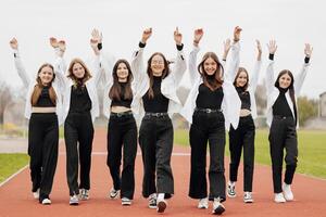 un' gruppo di molti contento adolescenziale ragazze vestito nel il stesso attrezzatura avendo divertimento e in posa nel un' stadio vicino un' Università. concetto di amicizia, momenti di felicità. scuola amicizia foto