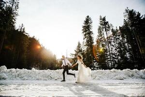 il sposa e sposo siamo in esecuzione lungo un' nevoso strada contro il sfondo di un' pino foresta e bellissimo contrasto luce del sole. lato Visualizza. inverno nozze. posto per logo. foto