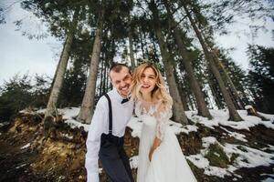 un' giovane coppia, il sposa e sposo, sorridendo mostrare via loro nozze anelli contro il sfondo di alto alberi. avere un' bene tempo ridendo. inverno nozze foto