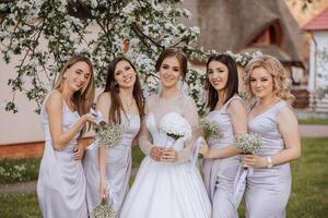 gruppo ritratto di il sposa e damigelle. un' sposa nel un' nozze vestito e damigelle d'onore nel argento vestiti hold elegante mazzi di fiori su loro nozze giorno. foto