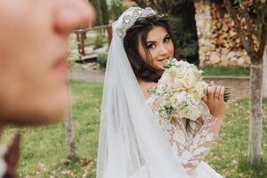 un' bello sposo nel il primavera foresta sta nel davanti di il suo sposa. bellissimo nozze bianca vestire. passeggiate nel il parco. un' contento e amorevole coppia. foto