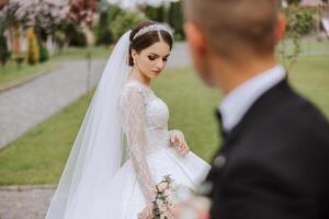 un' bellissimo giovane sposa, nel un' estate parco, passeggiate avanti di sua sposo. bellissimo nozze bianca vestire. passeggiate nel il parco. un' contento e amorevole coppia. foto