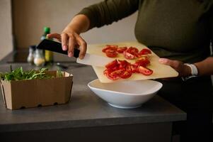 capocuoco mani con coltello, taglio rosso pomodori per insalata. fresco la verdura, rucola le foglie e oliva olio su il tavolo foto