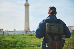 giovane maschio avventuriero turista in piedi indietro per telecamera, guardare a un' faro su il natura. viaggiare, attivo stile di vita foto