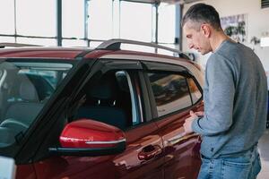 un' uomo esamina un' auto nel il cabina per difetti. auto affitto. acquisto un' auto foto