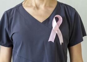 tiro di il femmina medico contro il bianca parete con rosa nastro, come un' simbolo di un' Seno cancro consapevolezza. concetto foto