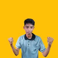 il entusiasta viso di il asiatico gioventù stretto il suo pugni. isolato su giallo sfondo. foto