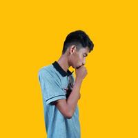 un asiatico uomo è copertura il suo bocca con il suo mani stretto in pugni Tenere il suo il petto, isolato su un' giallo sfondo foto