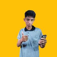 asiatico uomo sorridente viso con va bene gesto Tenere inteligente Telefono, isolato su blu sfondo foto