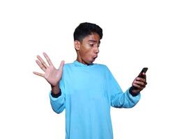 giovane asiatico uomo sorpreso guardare a mobile Telefono indossare blu maglietta, bianca sfondo foto