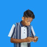 giovane asiatico uomo sorpreso guardare a inteligente Telefono nel sinistra mano Tenere isolato blu sfondo foto