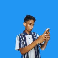 giovane asiatico uomo sorpreso guardare a inteligente Telefono nel sinistra mano Tenere isolato blu sfondo foto
