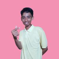 giovane asiatico uomo sensazione contento e romantico formatura cuore gesto, indossare giallo maglietta su rosa sfondo. foto