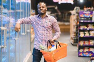 giovane africano uomo acquisto nel drogheria sezione a supermercato foto