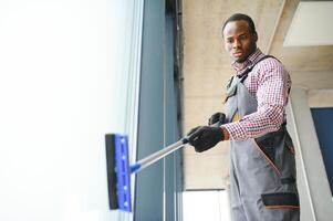 africano maschio professionale pulizia servizio lavoratore nel tuta da lavoro pulisce il finestre e negozio finestre di un' memorizzare con speciale attrezzatura foto