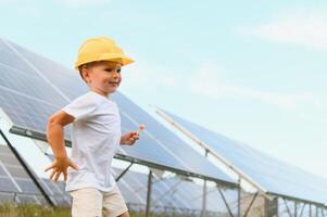 ritratto di un' bambino vicino il solare pannelli. un' poco ragazzo nel un' protettivo casco vicino solare pannelli con il suo mano. tiro a un' solare energia pianta. ecologico azienda agricola. solare energia stazione. persone foto