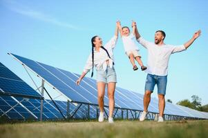 giovane famiglia con un' piccolo bambino nel sua braccia su un' sfondo di solare pannelli. un' uomo e un' donna Guarda a ogni altro con amore. solare energia concetto. foto