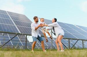 giovane famiglia di tre è accovacciato vicino fotovoltaico solare pannello, poco ragazzo e genitori. moderno famiglia concetto. il concetto di verde energia foto