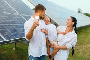 giovane famiglia di tre è accovacciato vicino fotovoltaico solare pannello, poco ragazzo e genitori. moderno famiglia concetto. il concetto di verde energia foto