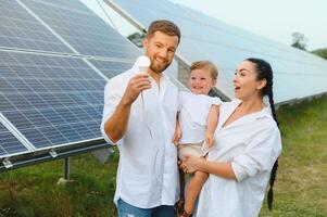 giovane famiglia di tre è accovacciato vicino fotovoltaico solare pannello, poco ragazzo e genitori. moderno famiglia concetto. il concetto di verde energia foto
