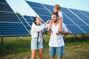 giovane famiglia di tre è accovacciato vicino fotovoltaico solare pannello, poco ragazzo e genitori. moderno famiglia concetto. il concetto di verde energia foto