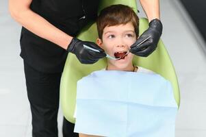 carino ragazzo sorridente mentre denti esame . contento ragazzo seduta nel dentisti sedia e avendo dai un'occhiata su denti foto