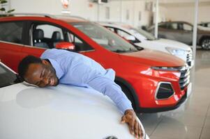 nuovo auto proprietario. contento africano americano uomo toccante abbracciare il suo nuovo di zecca auto foto