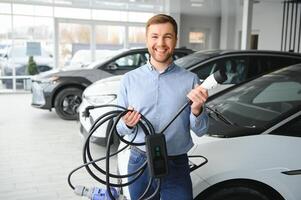 un' contento uomo sceglie un' nuovo elettrico auto a un' auto concessionaria. il concetto di acquisto un ecologico auto foto