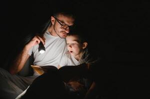 contento famiglia lettura di andare a dormire storia sotto coperta nel sera. padre e figlio trascorrere tempo insieme. Il padre di giorno foto