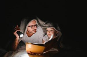 contento famiglia lettura di andare a dormire storia sotto coperta nel sera. padre e figlio trascorrere tempo insieme. Il padre di giorno foto