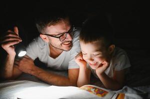 contento famiglia lettura di andare a dormire storia sotto coperta nel sera. padre e figlio trascorrere tempo insieme. Il padre di giorno foto