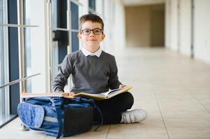 scolaro con cartella e libri nel il scuola. formazione scolastica concetto. indietro per scuola. schoolkid andando per classe. elegante ragazzo con zaino. ragazzo pronto per studia foto