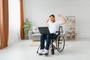 ritratto di sorridente Disabilitato maschio seduta nel sedia a rotelle e Lavorando su il computer portatile a partire dal casa. giovane lavoratore con speciale necessità. libero professionista e persone con disabilità concetto. foto