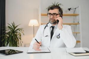 ritratto di anziano medico nel bianca cappotto a posto di lavoro. foto