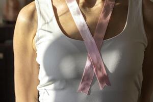 tiro di il donna nel il bianca superiore contro il bianca parete, con rosa nastro su sua collo come un' simbolo di Seno cancro consapevolezza. concetto foto