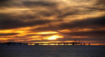 un' tramonto al di sopra di il mare con molo nel silhouette foto
