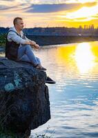 uomo contemplando della natura bellezza. un' uomo seduta su superiore di un' roccia Il prossimo per un' corpo di acqua foto