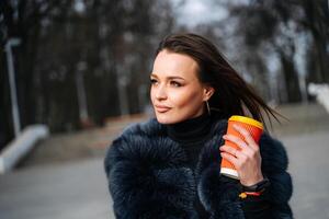 un' elegante donna nel un' pelliccia cappotto godendo un' tazza di caffè. un' donna nel un' pelliccia cappotto Tenere un' tazza di caffè foto