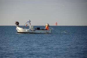 un' pescatore raccolta su il netto nel ligure mare pesca a partire dal piccolo barca foto