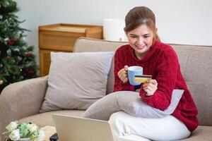 un' giovane asiatico donna con un' contento Sorridi detiene un' credito carta e usi un' smartphone per negozio in linea in linea pagamento concetto. foto