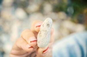 donna con manicure Tenere un' mare pietra nel dita nel luminosa sole leggero con forte bokeh foto